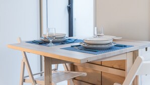 Ein Esstisch ist gedeckt mit Tellern, Gläsern und Besteck, mit einer blauen Tischmatte und einem hölzernen Stuhl.