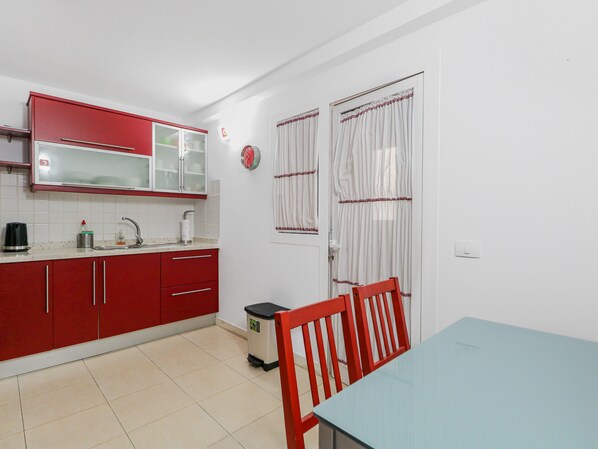 A compact kitchen with red cabinets, a sink, and a trash bin. - Macame house Puerto de las Nieves (Agaete)