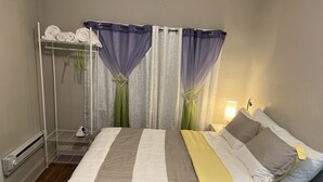 A neatly made bed with a striped bedspread, a bedside table with a lamp, and a window with sheer curtains.