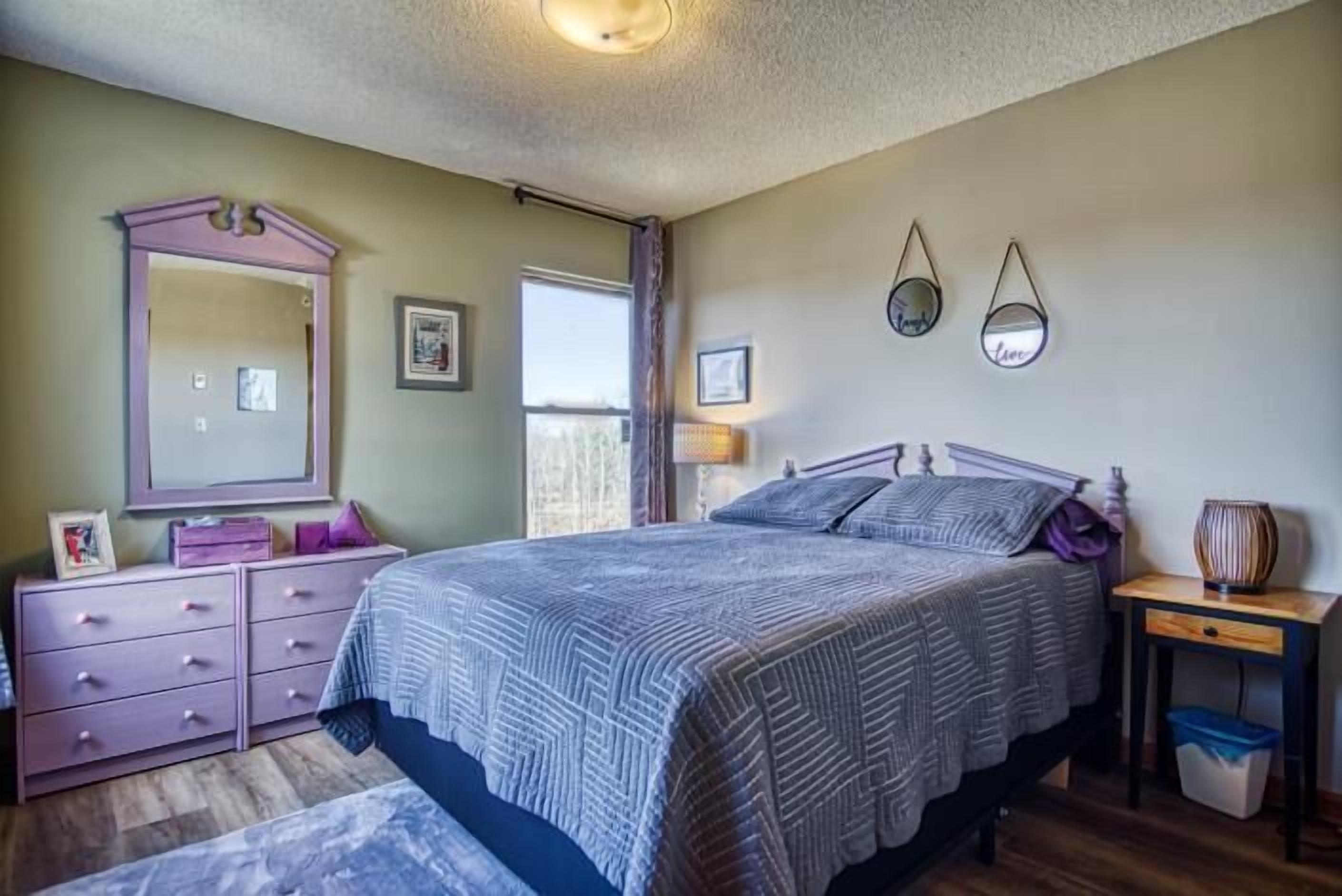 A bedroom with a bed, dresser, mirror, and bedside table.