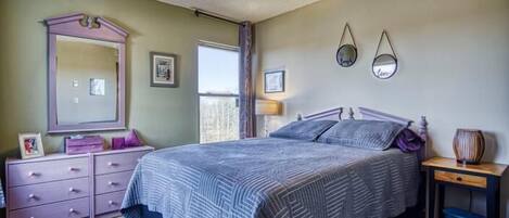 A bedroom with a bed, dresser, mirror, and bedside table.