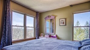 A bedroom with a large bed, a dresser, a mirror, and a window with a view of trees. - C302-Great views of lift! Slopeside Condo, pets OK! (Davis)
