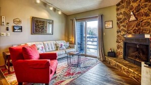 A living room with a stone fireplace, a sofa, a red armchair, and a large window. - C302-Great views of lift! Slopeside Condo, pets OK! (Davis)