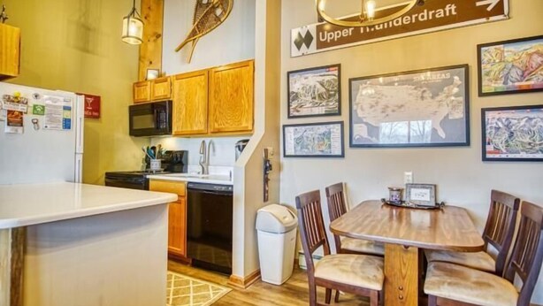 A kitchen with wooden cabinets, a white countertop, and a dining area with a wooden table and chairs. There are framed pictures on the wall and a sign indicating 'Upper Underdraft'. - C302-Great views of lift! Slopeside Condo, pets OK! (Davis)