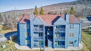 A two-story blue house with a central entrance, a fenced yard, and a mountainous backdrop. - C302-Great views of lift! Slopeside Condo, pets OK! (Davis)