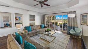 A spacious living room with a large sofa, a coffee table, and a ceiling fan. There is a sliding glass door leading to an outdoor patio area. - Centre Court Cay: Water Park, Golf View, Pool, Near Disney (Kissimmee)