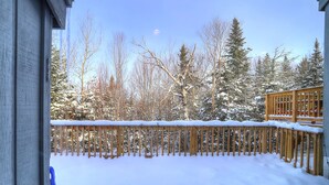 Una terraza de madera con barandillas cubiertas de nieve y árboles al fondo.