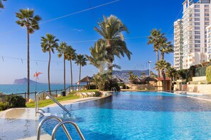 Ein Pool mit Liegestühlen, Palmen und Blick auf das Meer.