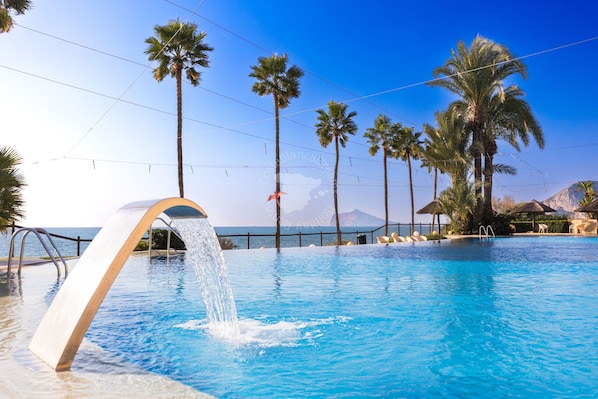 Piscina con fuente, palmeras y vista al océano.