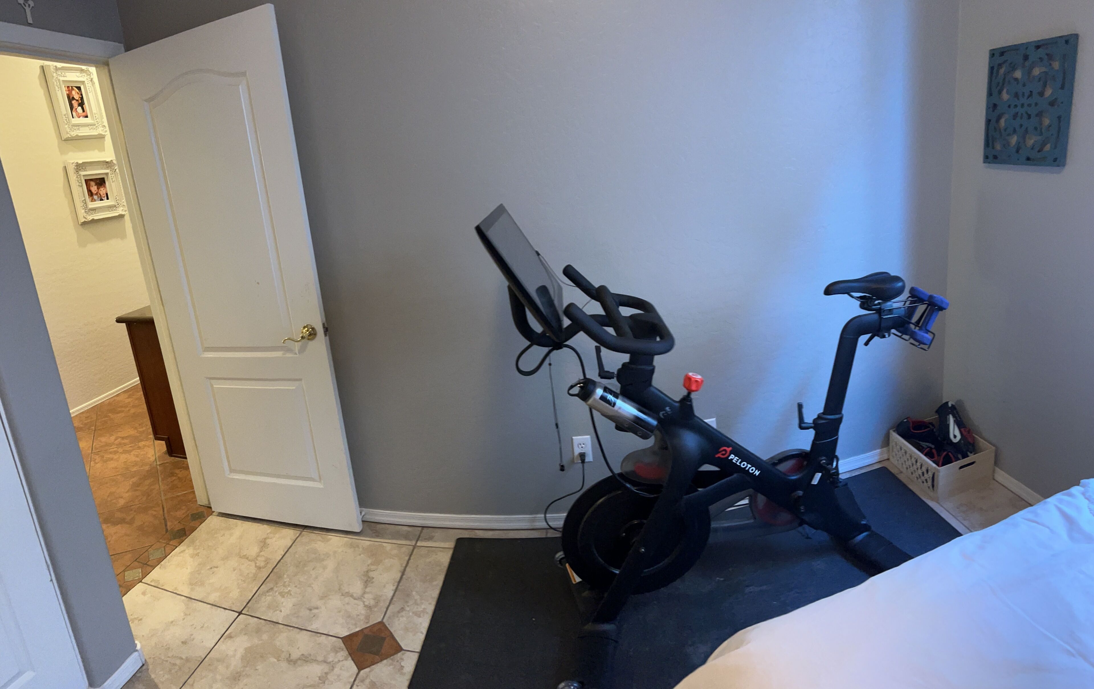 Une pièce comprenant un vélo d’appartement, un lit, une porte et un mur orné d’un cadre avec une image.