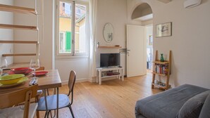Una sala de estar acogedora con una mesa de comedor de madera, sillas, un televisor sobre un mueble bajo, una estantería y un sofá.