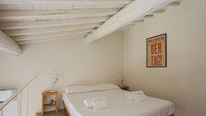 Un dormitorio con cama de madera, ropa de cama blanca, una mesita de noche con lámpara y un cartel en la pared.