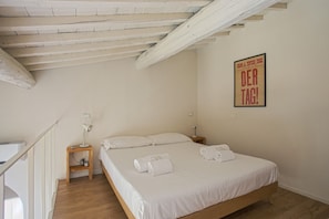 Ein Schlafzimmer mit einem hölzernen Bett, weißer Bettwäsche, einem Nachttisch mit Lampe und einem Bild an der Wand.