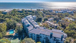 An aerial view of a coastal hotel with multiple buildings, a tennis court, and a swimming pool.