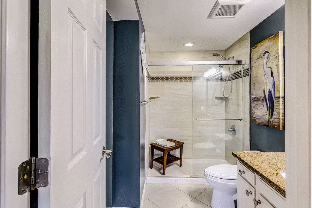 A bathroom with a glass shower enclosure, a toilet, and a small wooden stool.