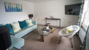 A living room with a sofa, a glass coffee table, a white chair, a TV, and a painting on the wall. - Franks- 2nd Floor Apt-2 Bath-Cowes Centre-Sleeps 4 (Isle of Wight)