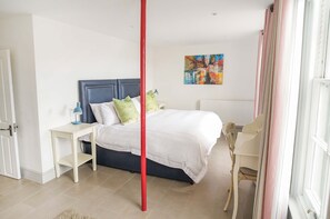 Un dormitorio con cama, mesita de noche, lámpara, silla y un cuadro en la pared.