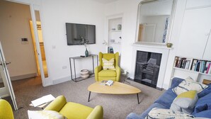 Ein Wohnzimmer mit einer Couch, Sesseln, einem Couchtisch, einem Kamin, einem Fernseher und einem Bücherregal.