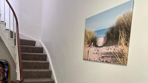 Eine Treppe mit Teppichstufen und einem Holzgeländer, die zu einer Empore mit einem Gemälde einer Strandansicht führt.