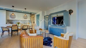 Una cocina moderna con armarios azules, una zona de comedor con sillas de mimbre y una sala de estar con muebles de madera.