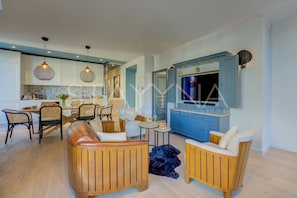 Eine moderne Küche mit blauen Schränken, ein Essbereich mit Korbstühlen und ein Wohnzimmer mit Holzmöbeln.