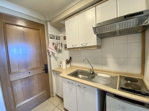 Una cocina con gabinetes blancos, un lavamanos de acero inoxidable, una campana extractora y un lavavajillas.