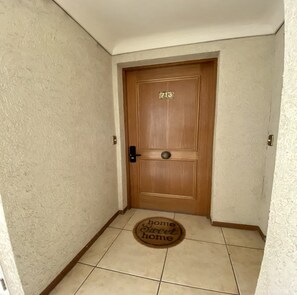Una puerta de madera con una placa de número, un felpudo y un interruptor de luz en la pared.