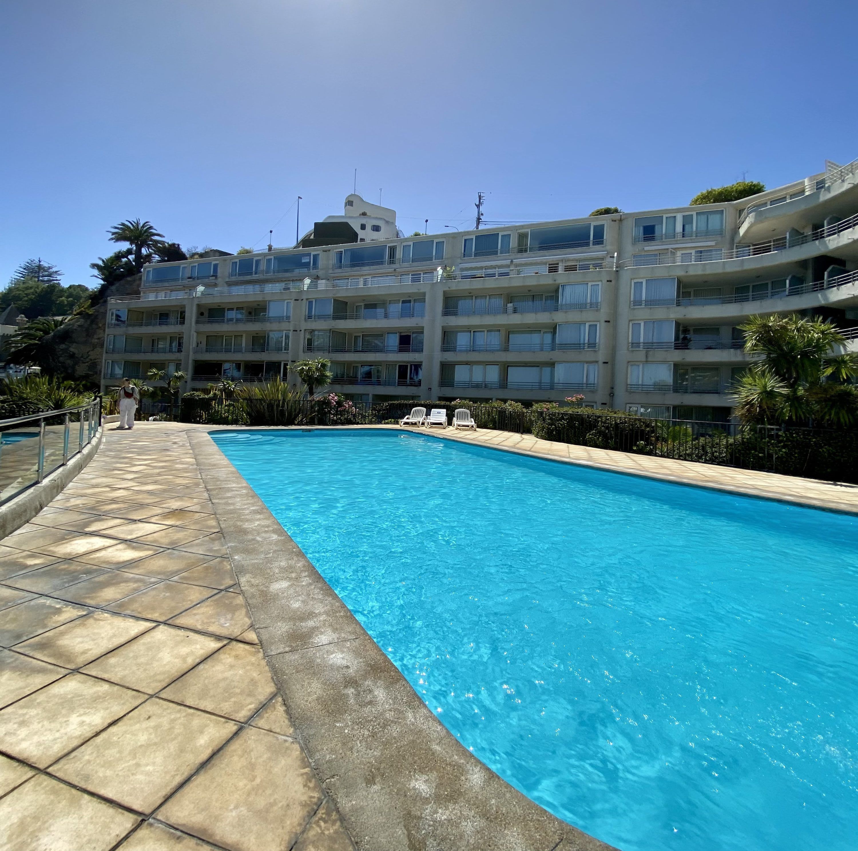 Una piscina con borde de baldosas, rodeada por un edificio de varios pisos con balcones.