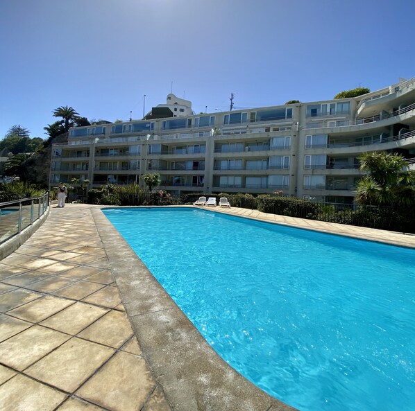 A swimming pool with a tiled deck, surrounded by a multi-story building with balconies. - Oceanfront Studio - A/C, Views, Pool & Parking (Viña del Mar)