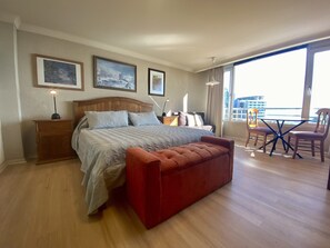 A bedroom with a bed, bedside tables, a red bench, a balcony with a table and chairs, and framed pictures on the wall.