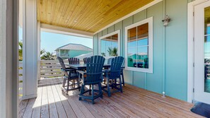 Eine überdachte Terrasse mit Holzdeck, einem Tisch und Stühlen sowie Blick auf ein Haus im Hintergrund.