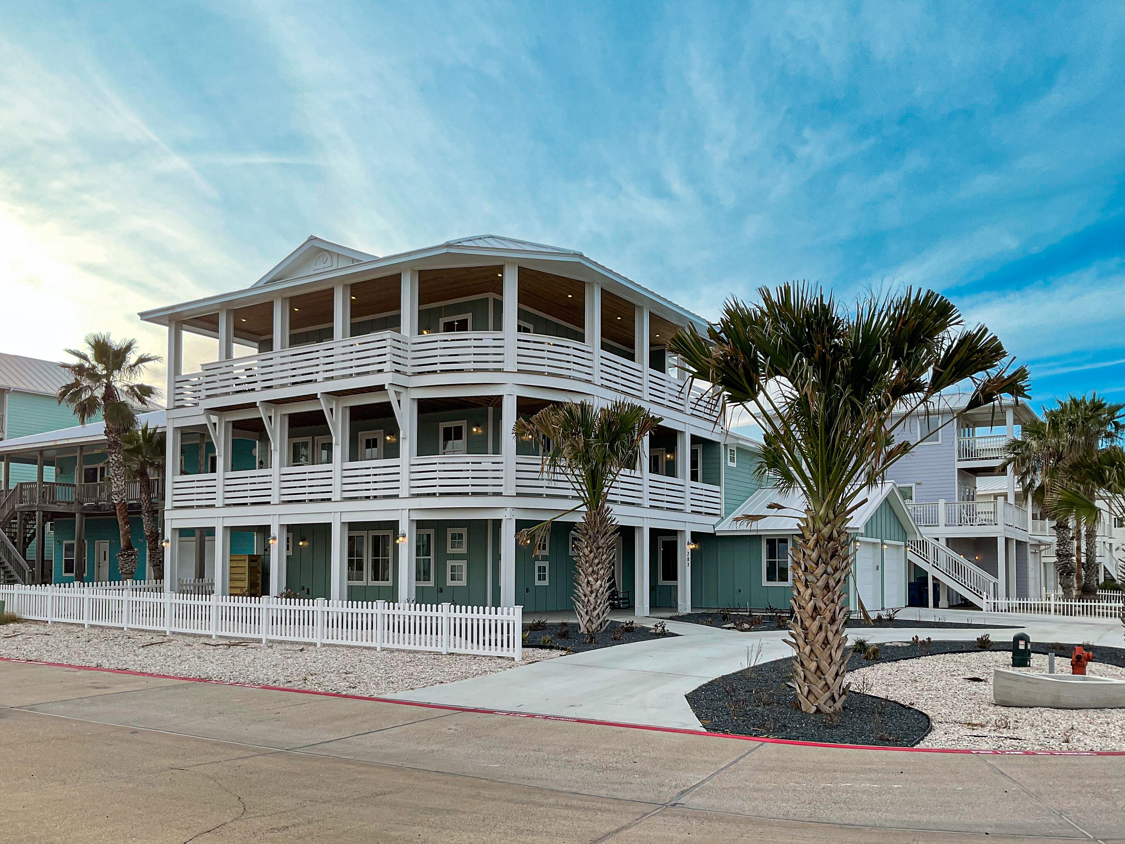 Un hôtel en bord de mer, avec plusieurs étages, des balcons, une clôture blanche et des palmiers.