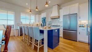 A modern kitchen with white cabinets, a blue island, stainless steel appliances, and a view to the outside. - Gulf Views, Private Heated Pool, Golf Cart Included, Boardwalk to the Beach (Port Aransas)