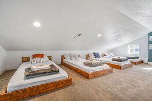 Ein Zimmer mit drei Betten aus Holz, die nebeneinander stehen, weißer Bettwäsche und einer schrägen Decke mit eingelassener Beleuchtung.