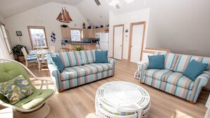 A spacious living area with striped sofas, a round wicker coffee table, and a dining table with chairs. - Oceanside, Private Pool, Hot Tub, Ocean Views (Rodanthe)