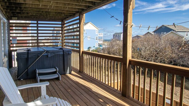 A wooden deck with two Adirondack chairs, a barbecue grill, and a view of houses in the background. - Oceanside, Private Pool, Hot Tub, Ocean Views (Rodanthe)