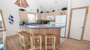 A kitchen with a central island, wooden bar stools, a microwave, and a refrigerator. - Oceanside, Private Pool, Hot Tub, Ocean Views (Rodanthe)