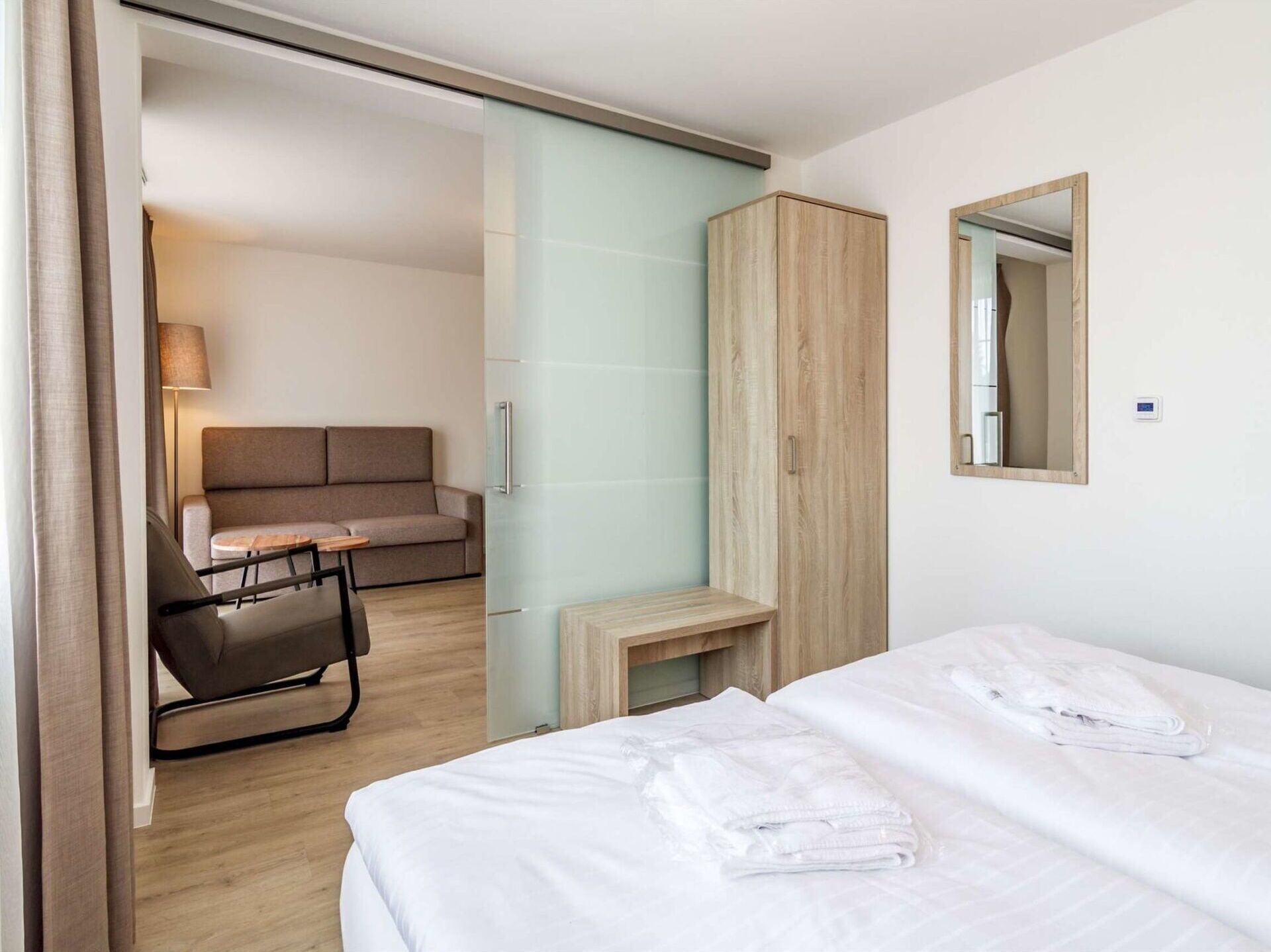A hotel room with a bed, a sofa, a desk, a wardrobe, and a mirror.