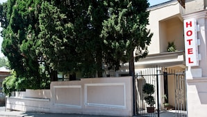 A hotel entrance with a large tree in front, a beige building, and a black gate. - Darchi Hotel (Tbilisi)