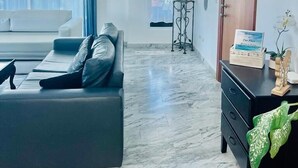 A modern living room with a black sofa, a wooden door, and a marble floor. - 2 Minutes Walk to Beach Huge 3 bdrm Condo with Pool (Punta Cana)