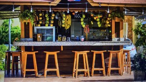 A restaurant with a tiled roof, outdoor seating with wooden stools, and hanging fruit decorations. - 2 Minutes Walk to Beach Huge 3 bdrm Condo with Pool (Punta Cana)