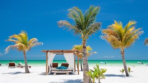 A beach with a wooden gazebo, lounge chairs, and a bed with a canopy.