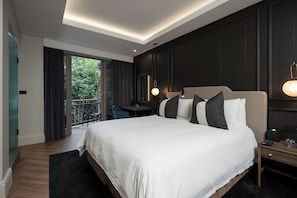 Une chambre d’hôtel moderne dotée d’un grand lit, d’un bureau et d’un balcon offrant une vue sur la verdure.