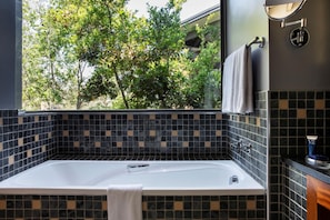 Un baño con bañera, una ventana con vista a árboles y un salpicadero de azulejos.