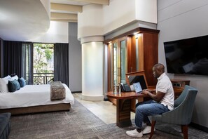 A hotel room with a bed, a desk with a laptop, a television, and a large window with curtains. - Seven Villa Hotel and Spa (Johannesburg)