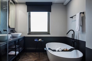 Un baño moderno con una bañera independiente, un espejo grande, una ventana y un tocador negro con lavamanos y estantes.
