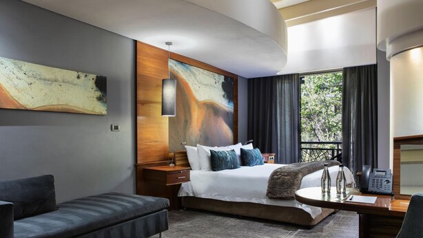 Habitación de hotel moderna con una cama grande, un sofá, un escritorio y vistas a zonas verdes.