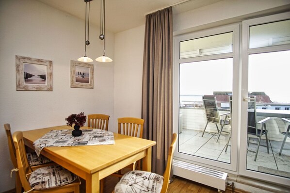 A dining area with a wooden table, four chairs, two pendant lights, and a large window with a view of buildings.