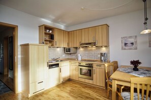 Una cocina compacta con armarios de madera, microondas integrado, lavavajillas y estufa. Hay una mesa de comedor con sillas y un jarrón con flores.