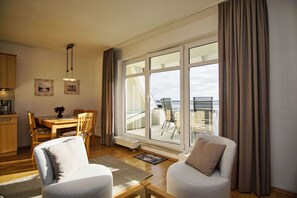 A modern living room with a dining area, large windows with curtains, and a view of the sea.